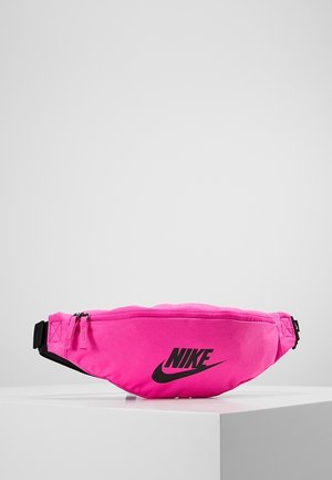 Jasnoróżowa nerka Nike z czarnym logo, główną kieszenią na suwak i regulowanym czarnym paskiem, wyeksponowana na białej platformie.