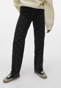 Svart denimbukser med hvite prikker, rett ben-design, middels høyde på livet, og et lett strukturert stoff. Kombinert med svarte og grå sneakers.