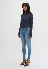 Navy long-sleeve shirt, light blue skinny jeans with zipper accents at the ankles, paired with black pointed-toe heels.