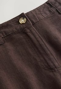 Bruine stoffen broek met een voorzak en een crème kleurige knoop aan de tailleband, met zichtbare stiksel details en een textuur oppervlak.