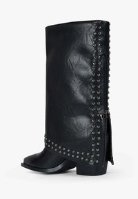 Stivali in ecopelle nera con un design morbido e accogliente, caratterizzati da dettagli con borchie d'argento lungo il lato esterno e una cerniera laterale per la chiusura.