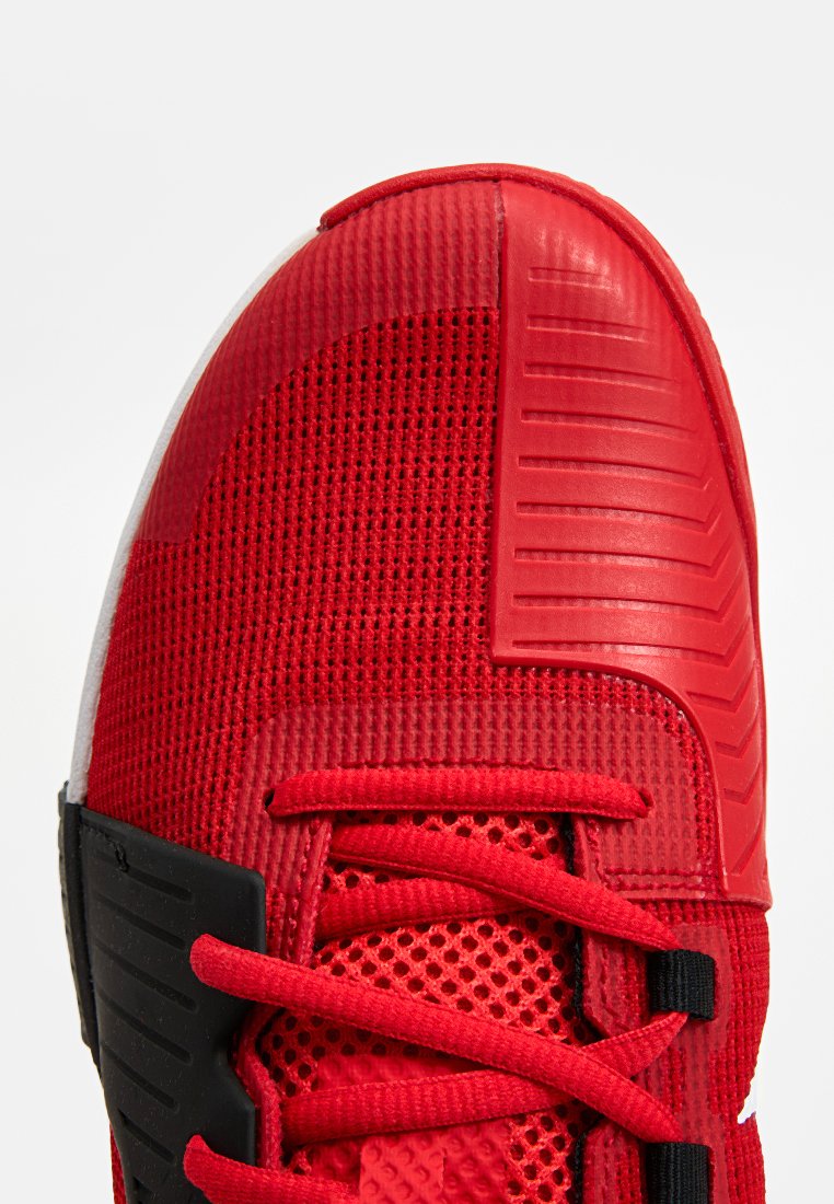 Rote Sportschuh mit strukturiertem Mesh-Obermaterial, Gummieinsätzen und flachen Schnürsenkeln. Die Zehenkappe hat eine glatte Oberfläche mit ausgeprägten Rillen.