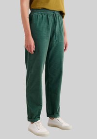 Grüne Baumwollhosen mit einem elastischen Taillenbund, Kordelzug, zwei Taschen, geradem Bein und einer leichten strukturierten Oberfläche, kombiniert mit weißen Sneakern.