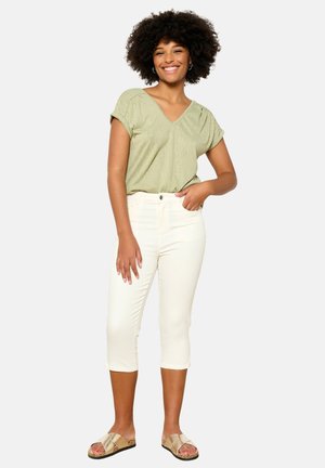 Top verde claro de cuello en V con mangas cortas, combinado con pantalones capri blancos. Modelo lleva sandalias de descanso beige con un diseño decorativo en la correa.