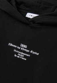 Zwarte katoenen hoodie met witte geborduurde tekst: "1996 L'Avenue des Champs-Élysées VII Arrondissement PARIS Île-de-France."