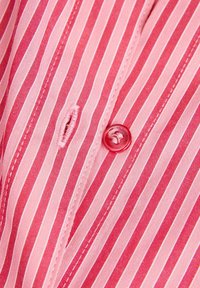 Pink and red striped fabric with a single button closure and buttonhole. The texture is smooth with stitched edges and a consistent pattern.