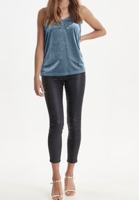 Blå sammetstopp med scallop-utskärning och blommig broderi, tillsammans med svarta åtsittande leggings i konstläder och beige sandaletter med remmar.