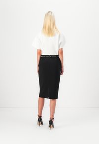 Svart blyantskjørt med splitt bak, kombinert med en hvit t-skjorte med korte ermer. Modellen har på seg svarte høyhælte sko. Minimalistisk design.