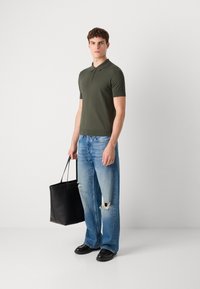 Olivenfarget kortermet polo skjorte, lyseblå slitte straight-leg jeans, svarte lærsko og en svart totebag.