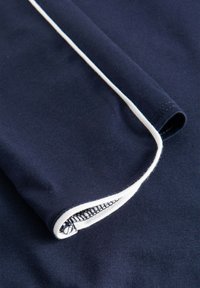 Marineblaues Material mit weißen Paspeln; weiche Textur; gefalteter Rand mit sauberer Naht und glattem Innenfinish.