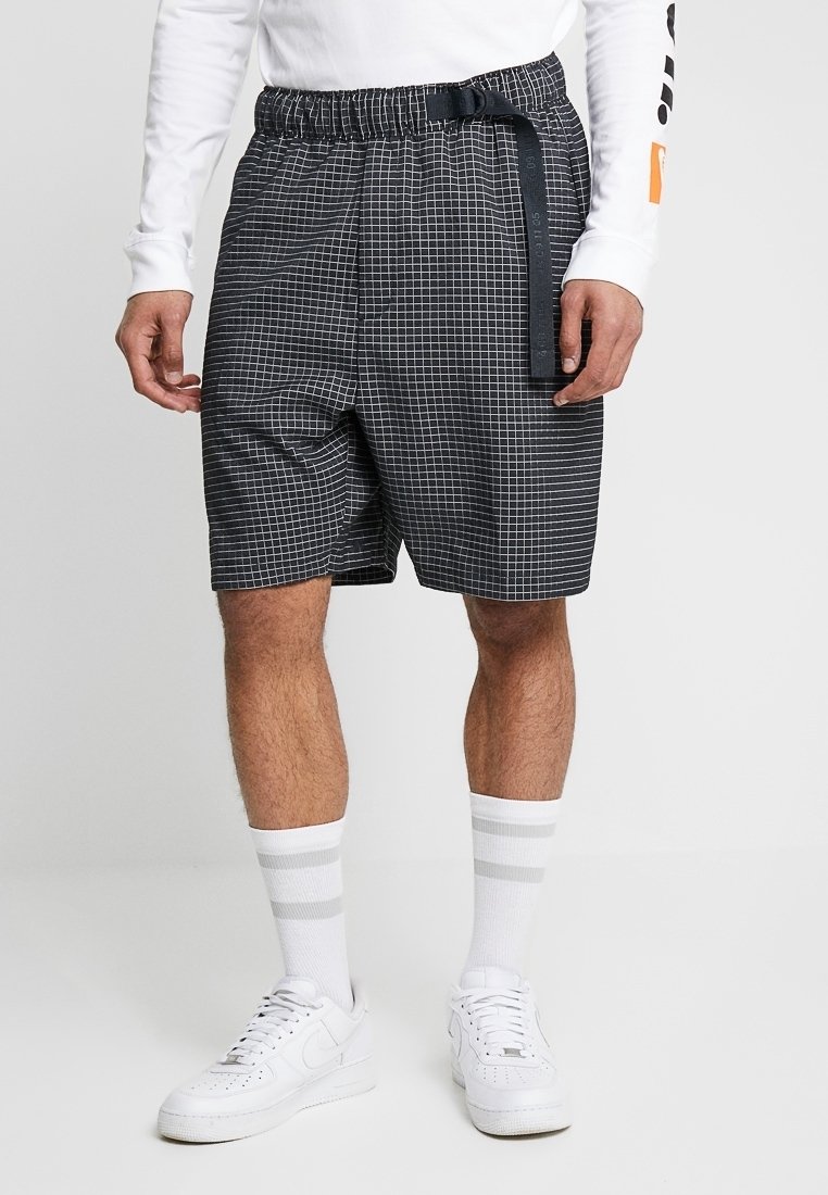 Mustat ja valkoiset ruudulliset shortsit, joissa on joustava vyötärö ja musta vyöyksityiskohta. Yhdistetty valkoisiin kenkiin ja raidallisiin sukkiin.