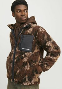 Brown plush fleece jacket with a camo pattern, zippered black chest pocket, and high collar. Features a soft texture and relaxed fit.