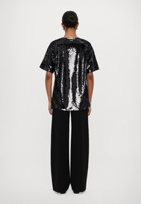 Black sequined short-sleeve top with a flowing design, paired with wide-leg black trousers. Smooth texture with reflective accents.