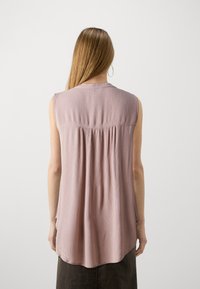 Blusa senza maniche in un leggero color malva, tessuto testurizzato con schiena arricciata, orlo arrotondato e dettagli di pieghe sottili.