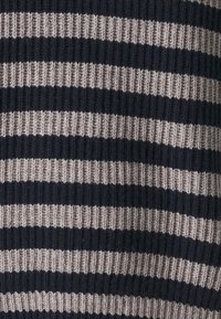 Neulottu villapaita, jossa on tummansinisiä ja beigejä vaakasuoria raitoja. Ominaisuuksina ribbitekstuuri ja vaihteleva raidan leveys kankaan kautta.