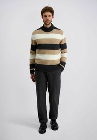 Gestreifter Pullover in Beige, Schwarz und Weiß, mit hohem Halsausschnitt und gerippten Bündchen; kombiniert mit dunklen, lässigen Hosen und schwarzen Schuhen.