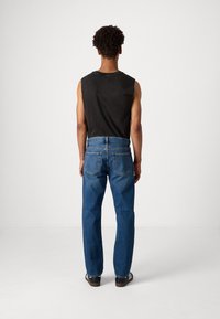 Top negro sin mangas combinado con jeans de mezclilla azules. Los jeans tienen un corte recto, un diseño de cinco bolsillos y detalles de costura visibles.