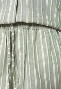 Tissu vert clair à rayures verticales blanches, montrant une taille élastique froissée avec cordon de serrage d'un vêtement.