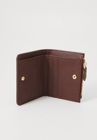 Portefeuille en cuir bordeaux avec surface texturée, comportant des emplacements pour cartes et un compartiment zippé. Accessoires en métal doré.