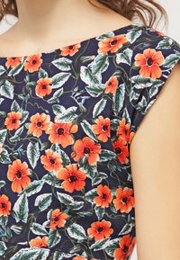 Květinové šaty s námořnickým pozadím, na kterém se vyjímají živé oranžové květy a zelené listy, jemný materiál a design s krátkým rukávem.