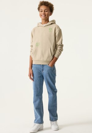 Beige hoodie met groene grafische print en zak, gecombineerd met lichtblauwe jeans en witte sneakers. Casual, ontspannen pasvorm.