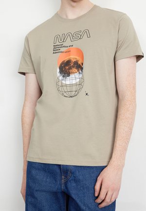 Camiseta de algodón beige con el logo de la NASA y un gráfico de la Tierra en un círculo naranja, ilustración de un globo negro, mangas cortas y cuello redondo.