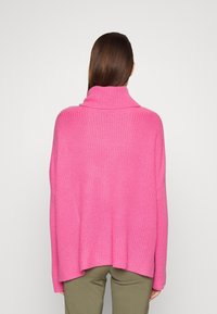 Maglione fucsia lavorato a maglia con collo alto a risvolto, maniche lunghe e vestibilità comoda, abbinato a pantaloni verde oliva.