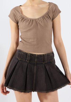 Bruine geribbelde top met korte mouwen en een geplooide halslijn, gecombineerd met een donker denim geplooide rok met rafelige zoom en gele stikseldetails.