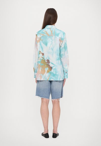 Langsleeve shirt in een pastel, abstracte print met tinten blauw, roze en bruin, gemaakt van glanzende stof; gecombineerd met denimshorts.
