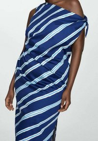 Robe asymétrique bleu marine à rayures blanches et bleu clair, avec une taille froncée, un détail noué sur l'épaule, et un ourlet asymétrique.