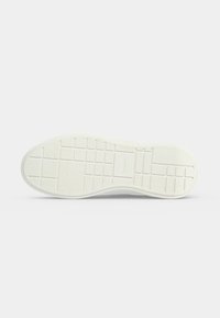 Semelle de chaussure blanche avec un motif en grille et des sections rectangulaires texturées de différentes tailles sur un fond neutre.