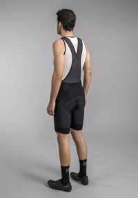 Black cycling bib shorts with mesh straps, featuring a padded seat and textured fabric. Includes elastic leg bands and fitted design.