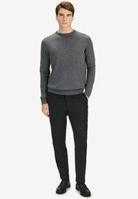 Grå stickad tröja med rund hals, i kombination med svarta byxor. Outfitten har en slim fit och kompletteras av svarta skor.