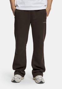 Bruna, avslappnade sweatpants med sidofickor och en diskret logotyp på vänster sida. Tillverkade av mjukt, texturerat tyg.