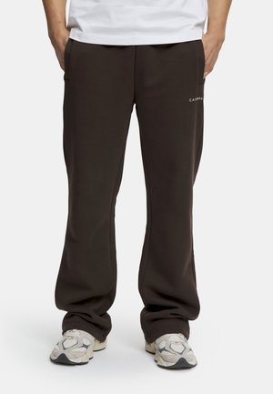 Brune, avslappede joggebukser med sidelommer og en subtil logo på venstre side. Laget av mykt, teksturert stoff.