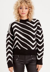 Pull noir et blanc à motif zigzag avec un col et un ourlet côtelés. Tricot doux et texturé avec une coupe surdimensionnée et des manches longues.