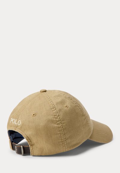 Μπεζ υφασμάτινο καπέλο μπέιζμπολ με ρυθμιζόμενο δερμάτινο λουράκι και λευκή κεντημένη λέξη "POLO" στο πίσω μέρος, εμφανιζόμενο από την πίσω δεξιά πλευρά σε λευκό φόντο.