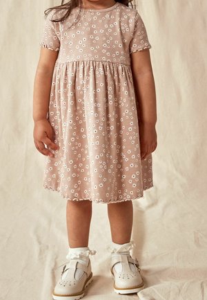 Robe en coton rose clair avec des manches courtes, texture côtelée, motif floral blanc, taille froncée et ourlet en feston. Chaussures blanches avec des chaussettes à volants.
