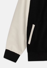 Black and cream sweatshirt with a leather sleeve and ribbed hem. Features a side pocket with a subtle horizontal seam detail.