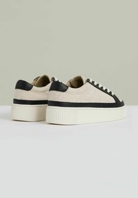 Beige canvas sneakers met zwarte accenten, met een gestructureerde afwerking, ronde neus en witte rubberen zolen met ribbeldetails.