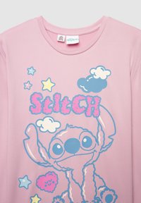 T-shirt in cotone rosa con grafica di un personaggio dei cartoni animati blu e rosa, accompagnato da stelle e nuvole. Collo rotondo e vestibilità rilassata.