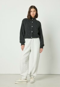 Cardigan tricoté gris foncé avec un col montant et des boutons à l'avant, assorti à un jogging gris clair et des baskets beiges. Texture lisse.