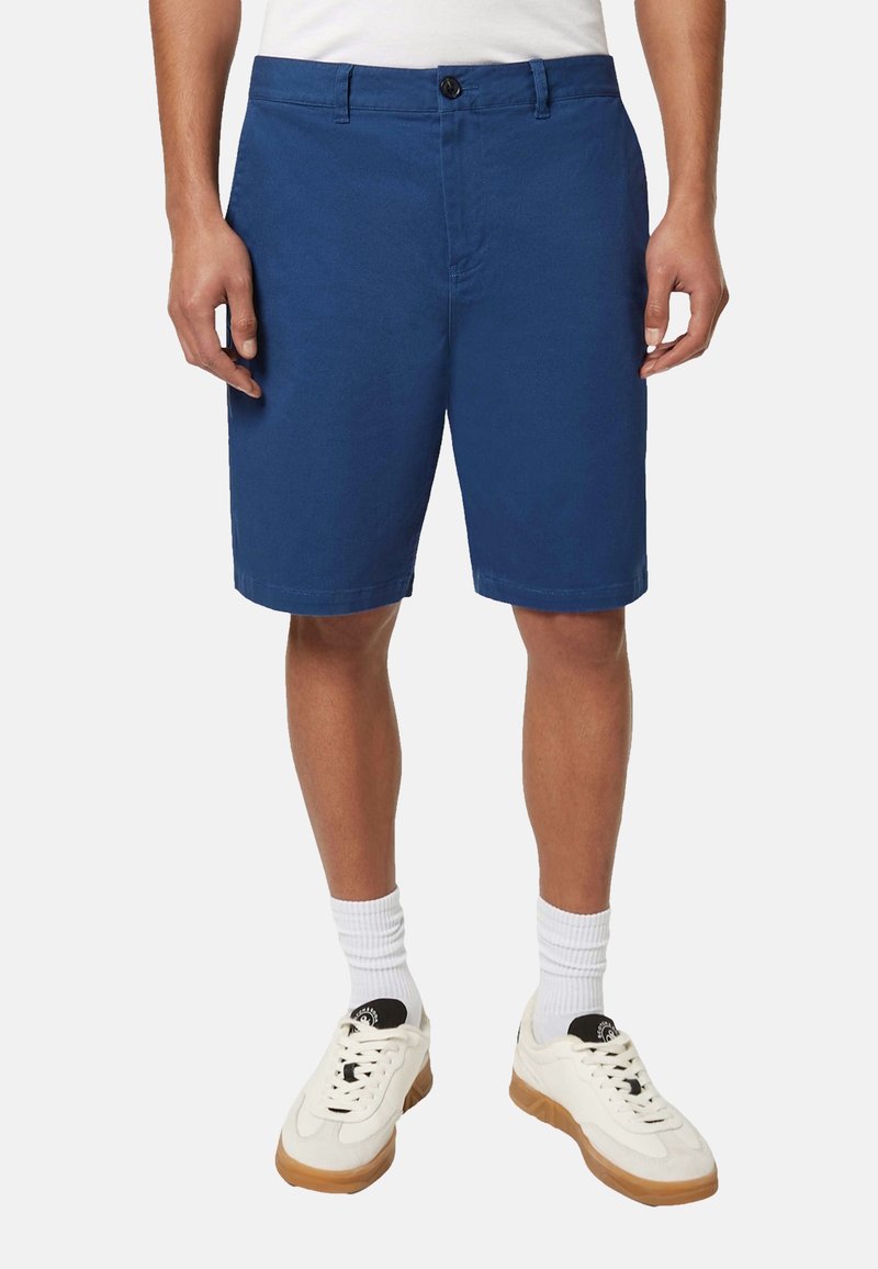 Blå bomulds-shorts med lige snit, enkelt knaplukning, sidelommer og en ren kant. Kombination med hvide sokker og sneakers.