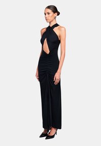 Abito nero senza maniche con scollo halter, dettaglio cut-out anteriore, arricciature lungo i lati e una silhouette aderente, abbinato a tacchi neri.