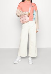 Suéter multicolor con media cremallera, que presenta secciones en rosa, azul y beige; combinado con pantalones anchos blancos y un bolso cruzado rosa.