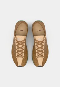 Baskets tan en cuir perforé, accents beige, semelle verte et lacets marron. Présente un logo "Nike Air" sur la languette.