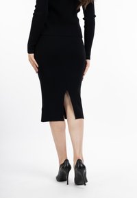 Rochie tricotată neagră, cu o fanta pe lateral, având o formă ajustată și concepută pentru o siluetă elegantă, completată de tocuri înalte negre.