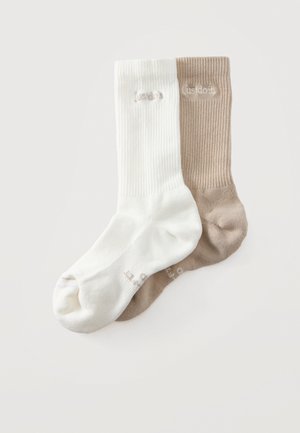 Une chaussette mi-mollet blanche et une taupe, toutes deux côtelées et ornées d’un logo brodé, sont présentées en se chevauchant sur un fond clair.