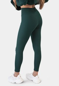 Groene geribde leggings met een hoge tailleband, een aansluitende vorm en enkellange stijl, gecombineerd met witte chunky sneakers.