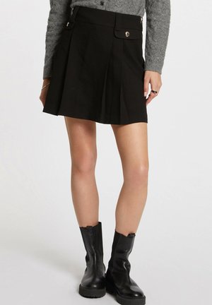 Black pleated skirt with a high waist, featuring side pockets and a smooth texture. Paired with knee-high black leather boots.